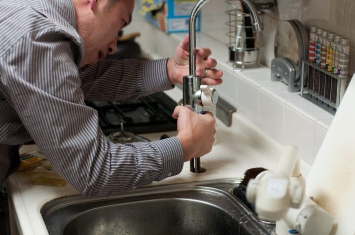 un propriétaire de maison se demandant comment déboucher une canalisation pleine de sable et utilisant un serpentin de plombier pour y arriver dans sa cuisine